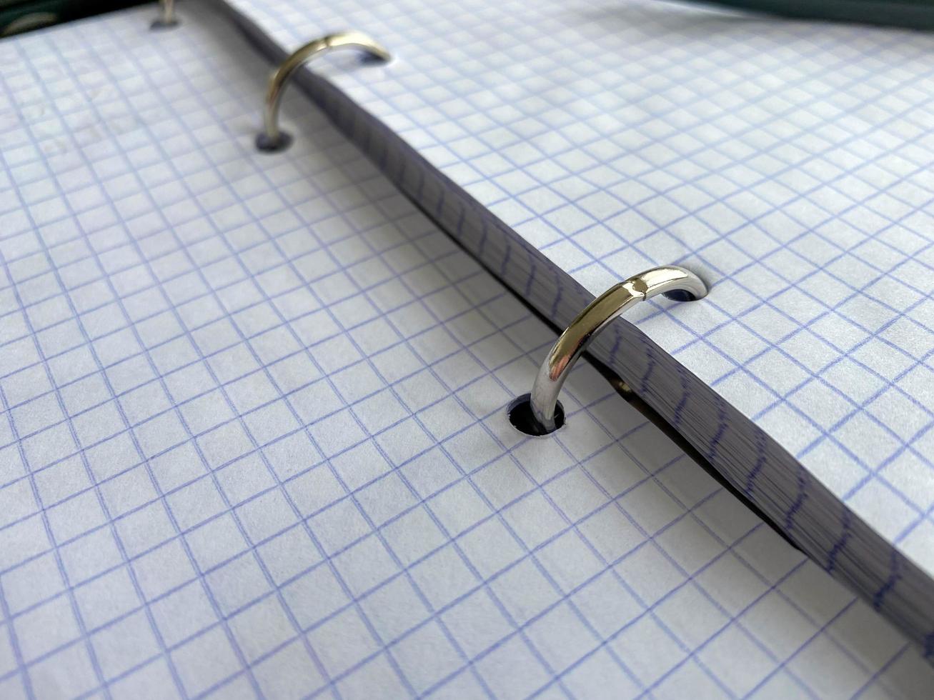 A writing pen rests on a notepad with squared paper sheets on a work desk with stationery in a business office photo