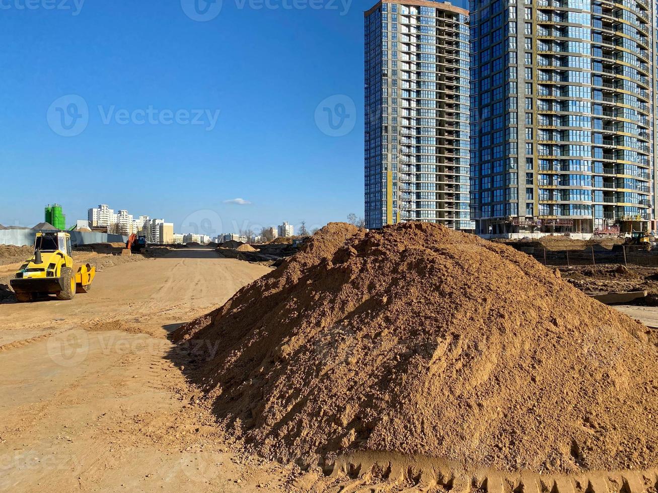 A large pile of yellow sand for the repair and construction of tall new buildings and structures of houses. New construction machinery and equipment at the construction site photo