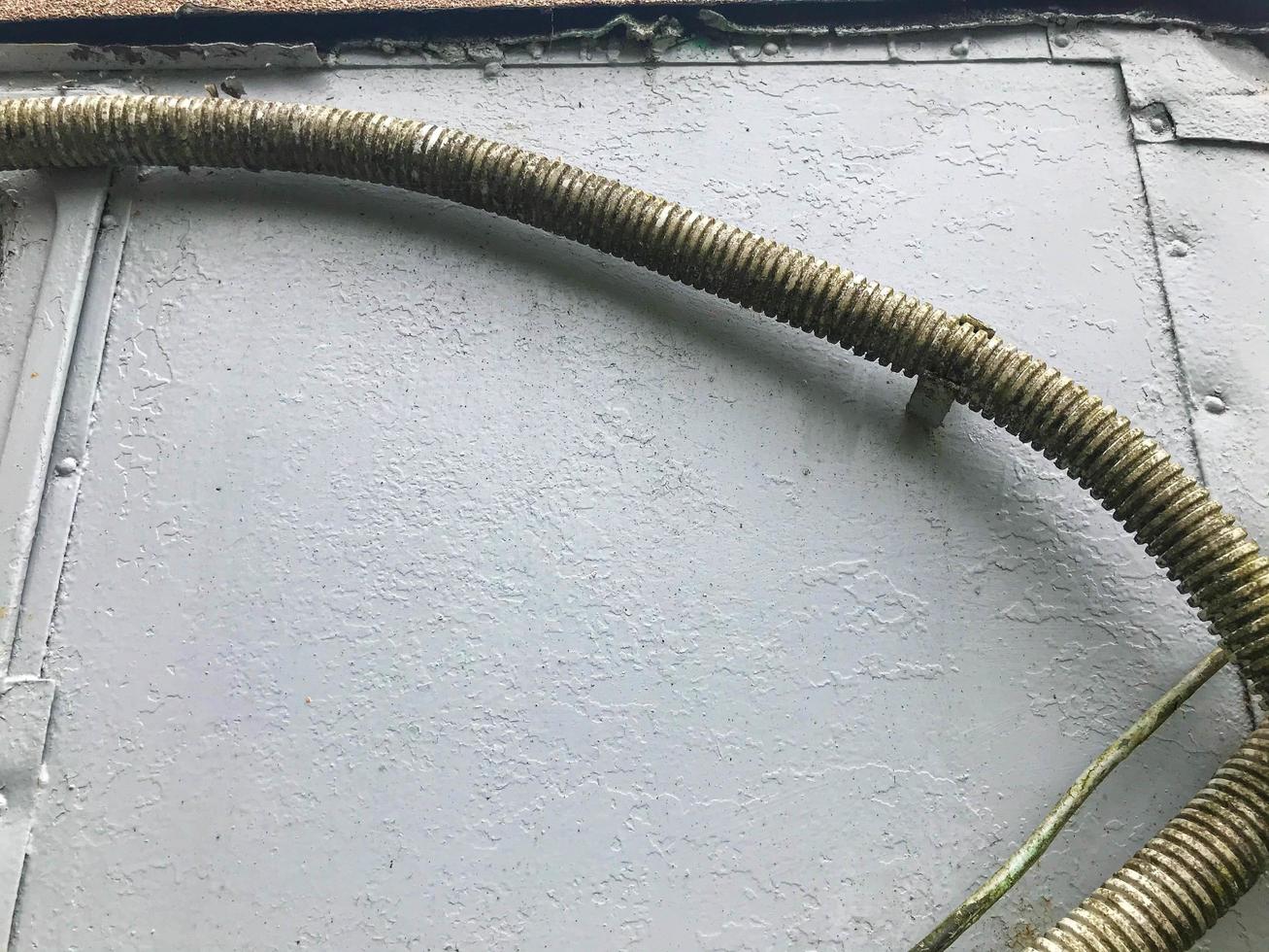 thick gray-green wires hang from a gray metal sheet. wires for transmitting electricity to the house. homemade power lines. moss and grass appeared on the wires photo