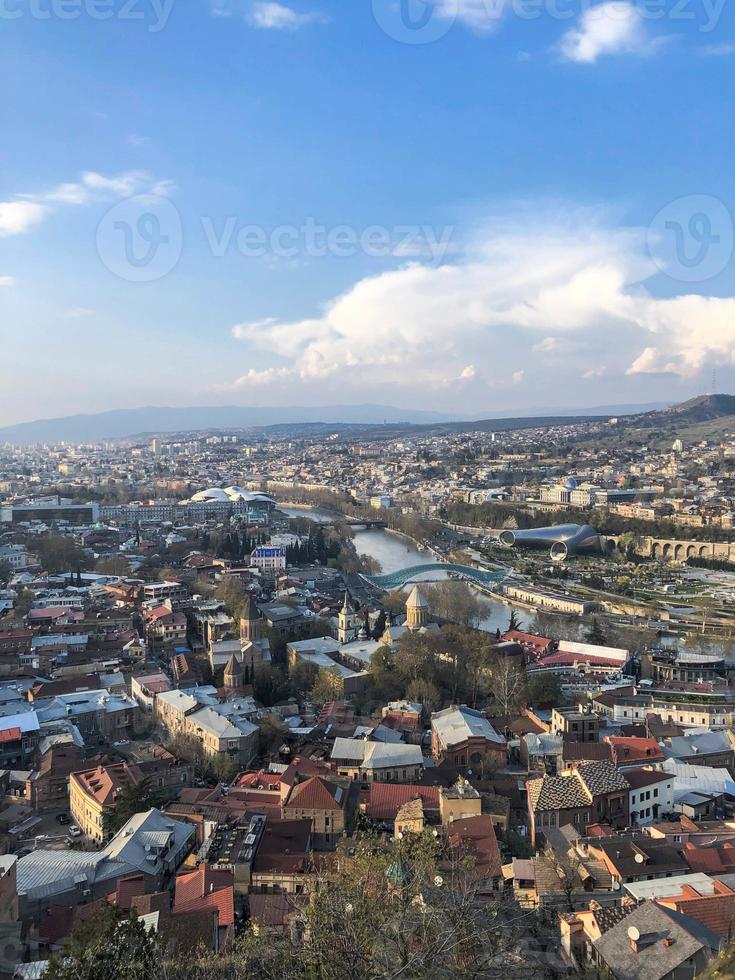 vista vertical desde lo alto de una hermosa ciudad turística con edificios y casas, techos de árboles y plantas, naturaleza contra el cielo azul y montañas. arquitectura antigua europea foto