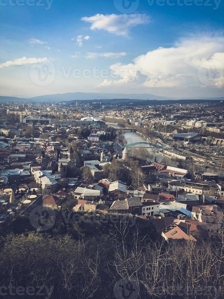 Vertical view from the top from a height of a beautiful tourist city with buildings and houses, roofs of trees and plants, nature against the blue sky and mountains. European old architecture photo
