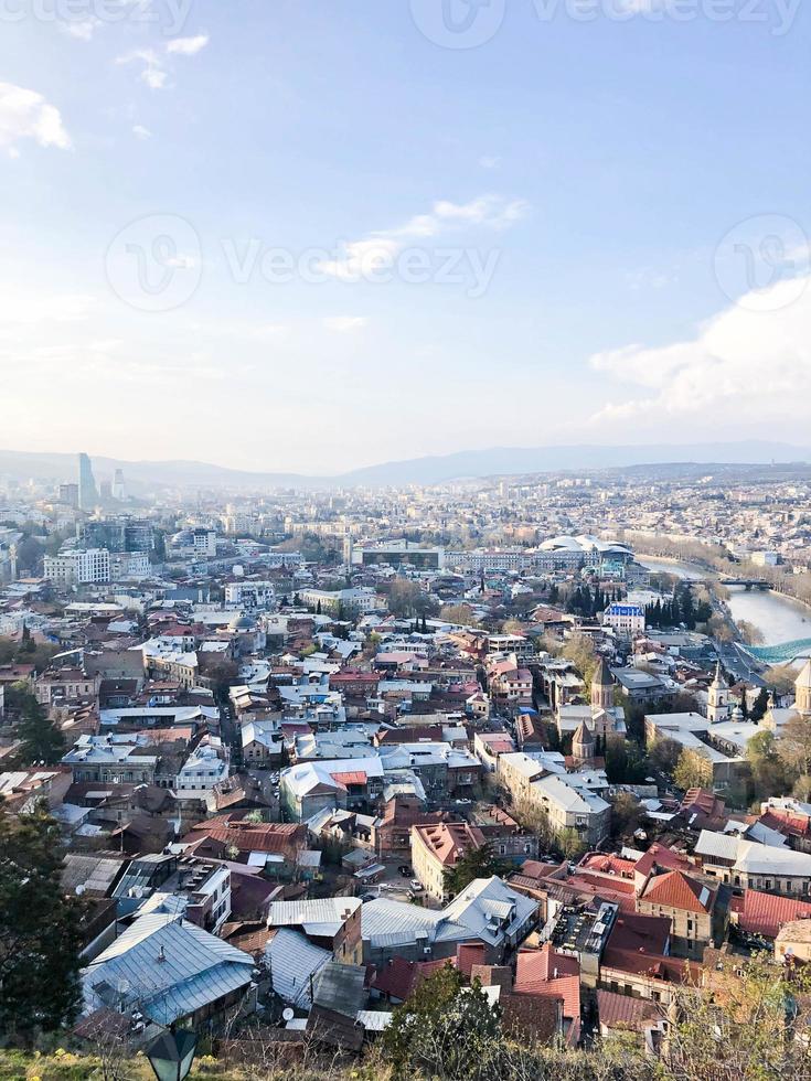 Vertical view from the top from a height of a beautiful tourist city with buildings and houses, roofs of trees and plants, nature against the blue sky and mountains. European old architecture photo