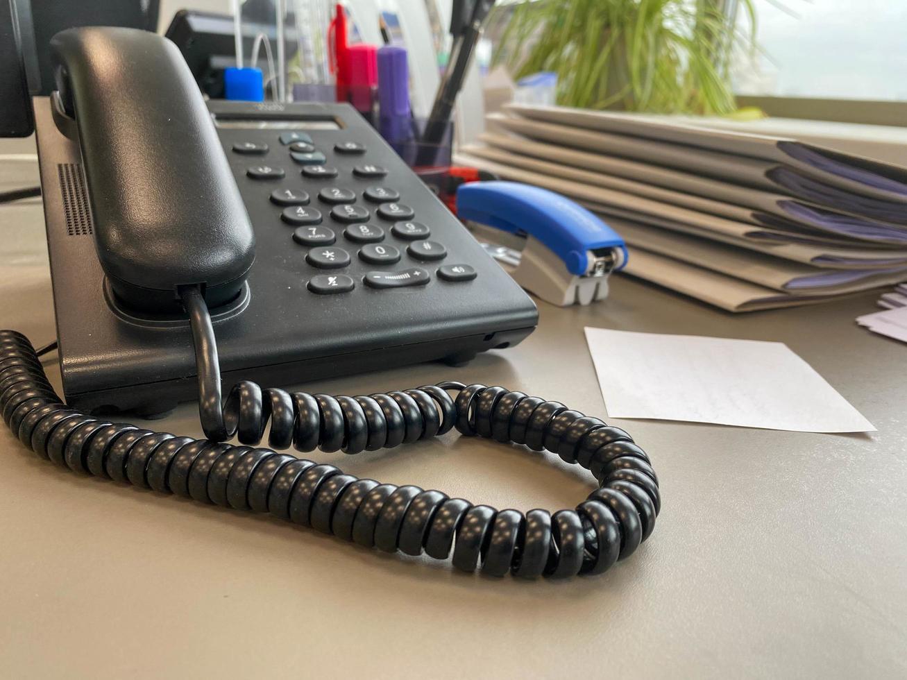 black wired phone on the desk next to a laptop in office desk photo