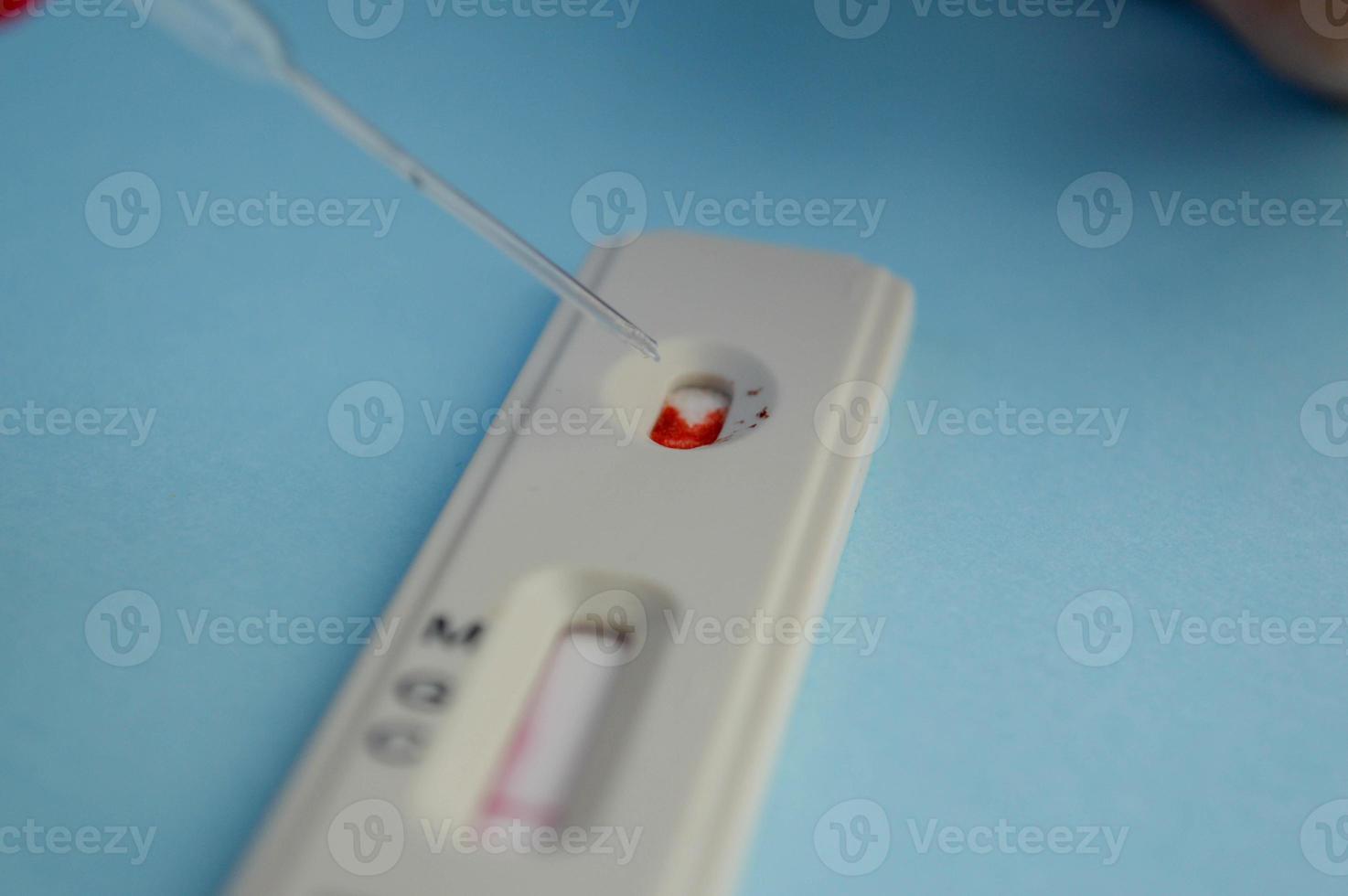 test for coronavirus on a blue background. girl with a bright red manicure makes a blood test. she adds a physical solution to a drop of blood for correct results photo