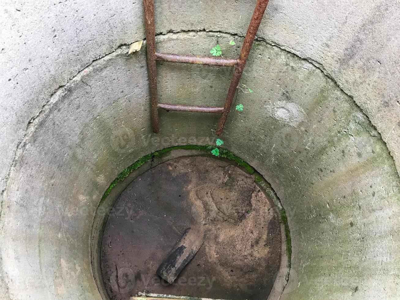 homemade well. concrete rings are installed in the courtyard of the house to extract resources from the ground. moss grows inside and there is a rusty staircase. abandoned well photo