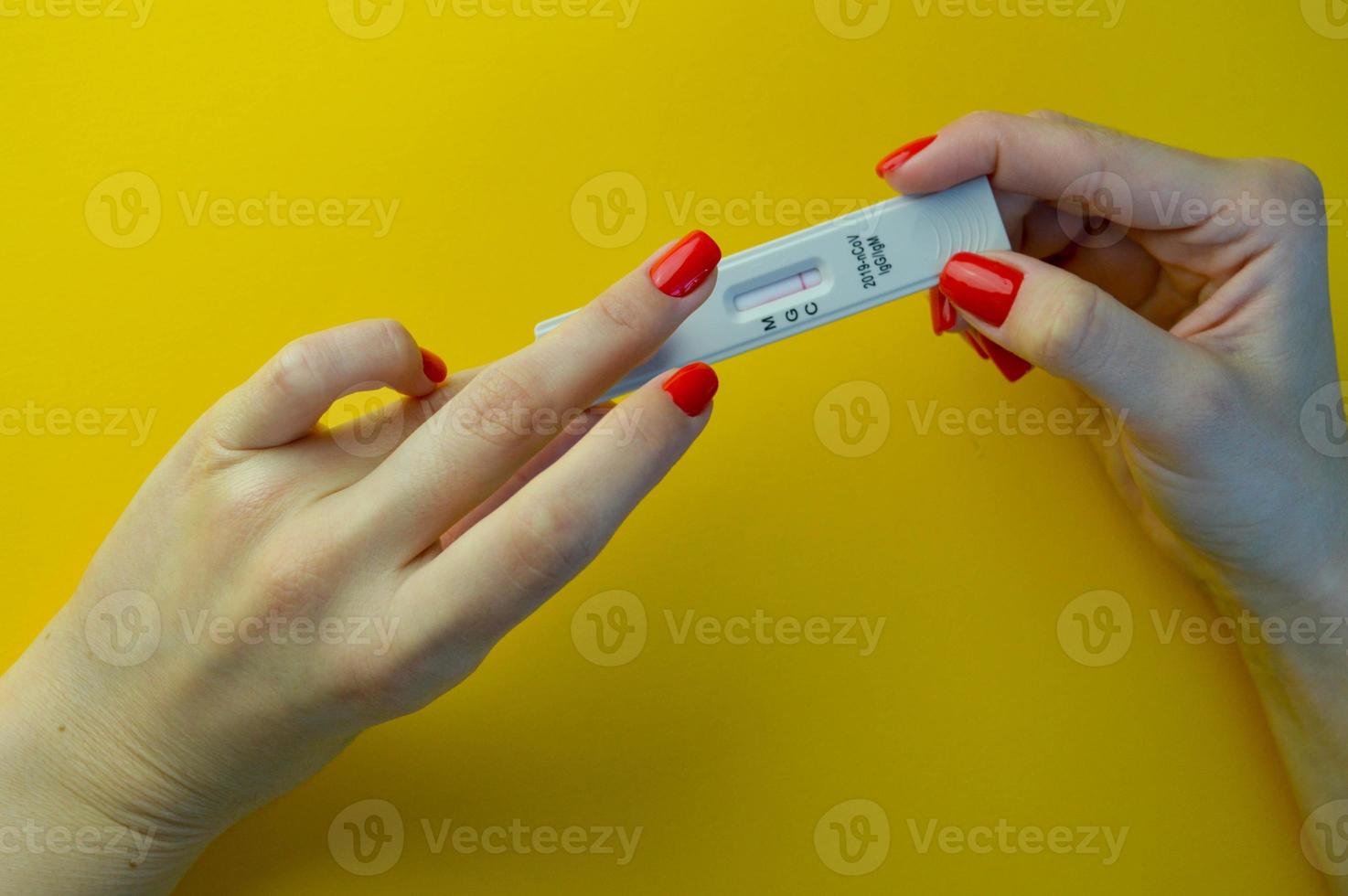 coronavirus test on a yellow, bright background. medical analysis. girl with bright red manicure holding a test strip. there is a strip on the window with the result, there are no antibodies photo