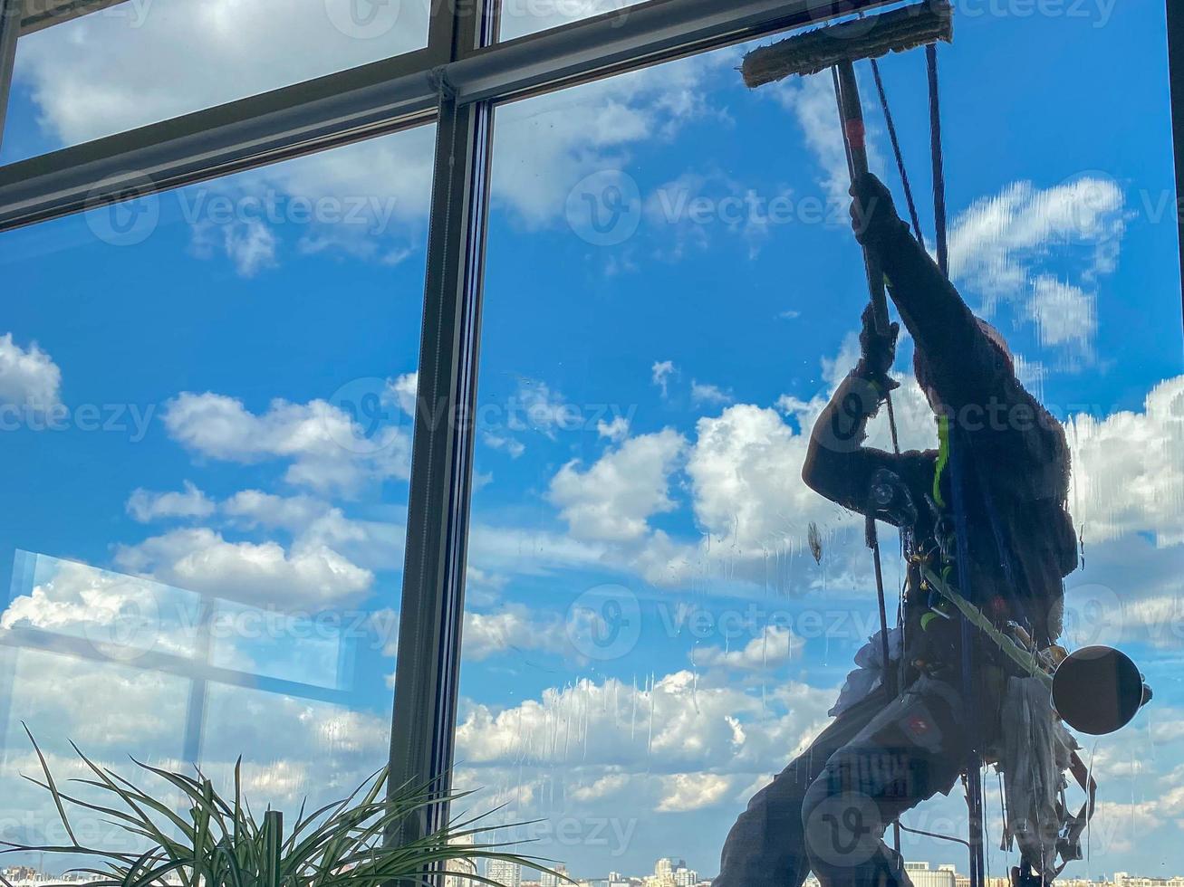 A male window washer worker, industrial climber hangs from a tall building, skyscraper and washes large glass windows for cleanliness high above a large city photo
