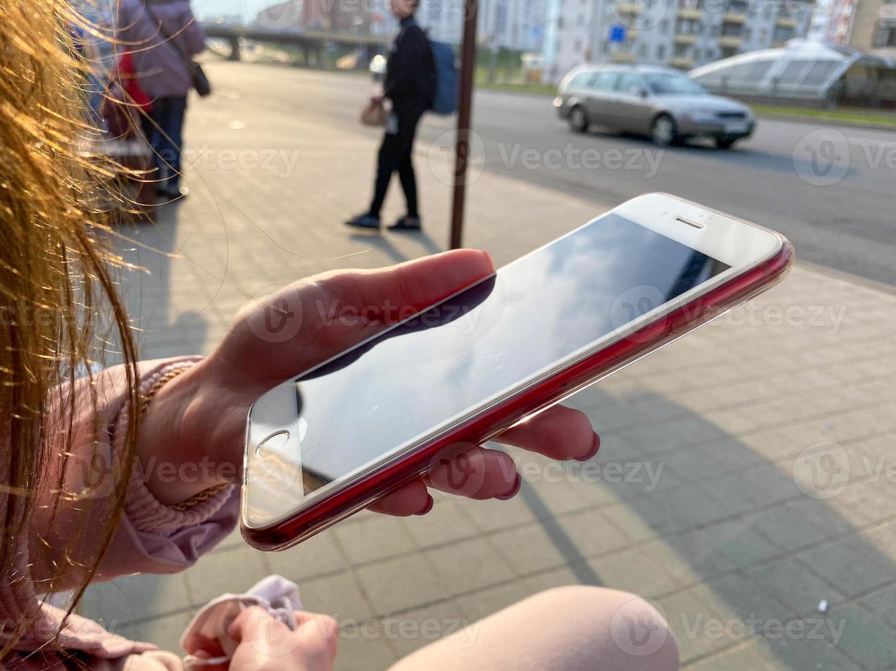 Beautiful girl woman sitting and holding a modern white mobile phone smartphone in her hand with fingers with a beautiful manicure on the street photo