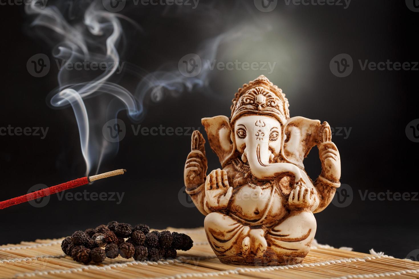 dios hindú ganesh sobre un fondo negro. estatua de rudraksha y rosario sobre una mesa de madera con un palo de incienso rojo y humo de incienso foto