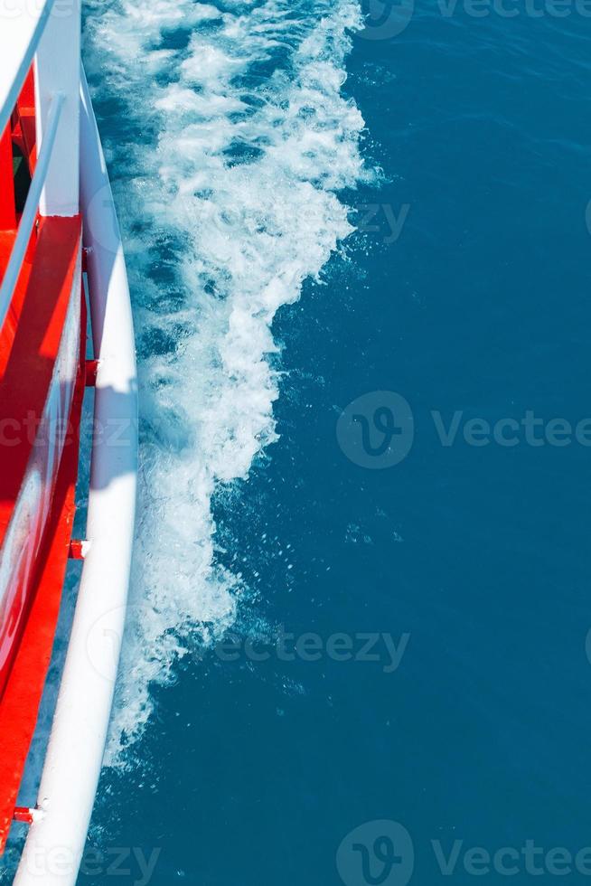 The red side of the cruise ship cuts through the blue sea surface, leaving the waves photo