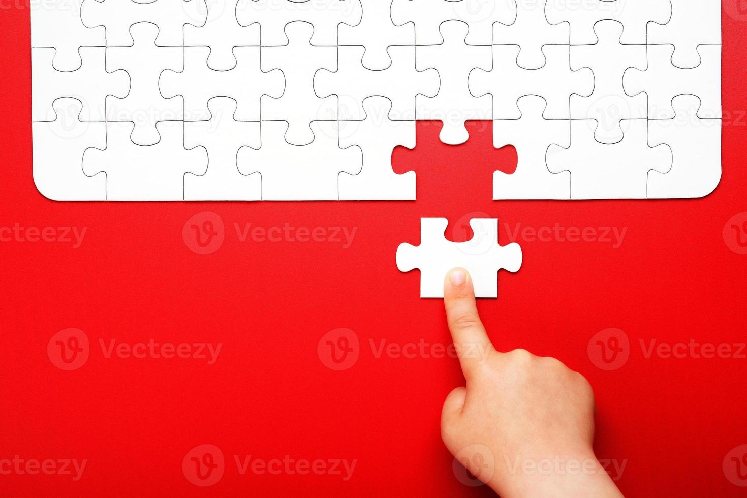 Children's hand moves a piece of white puzzle on a red background photo