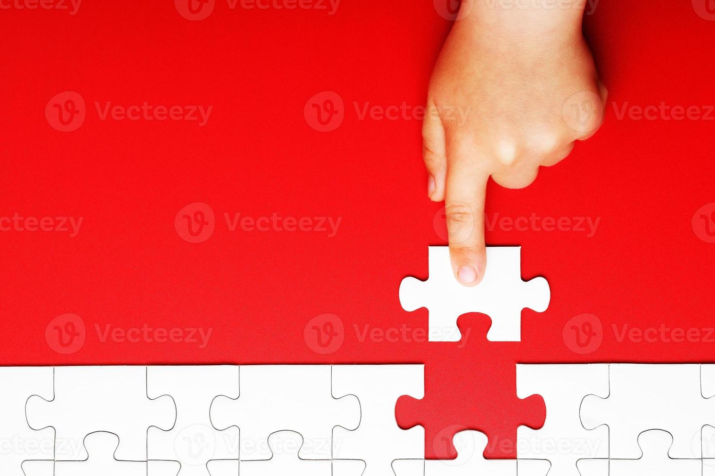 la mano de los niños mueve una pieza de rompecabezas blanco sobre un fondo rojo foto