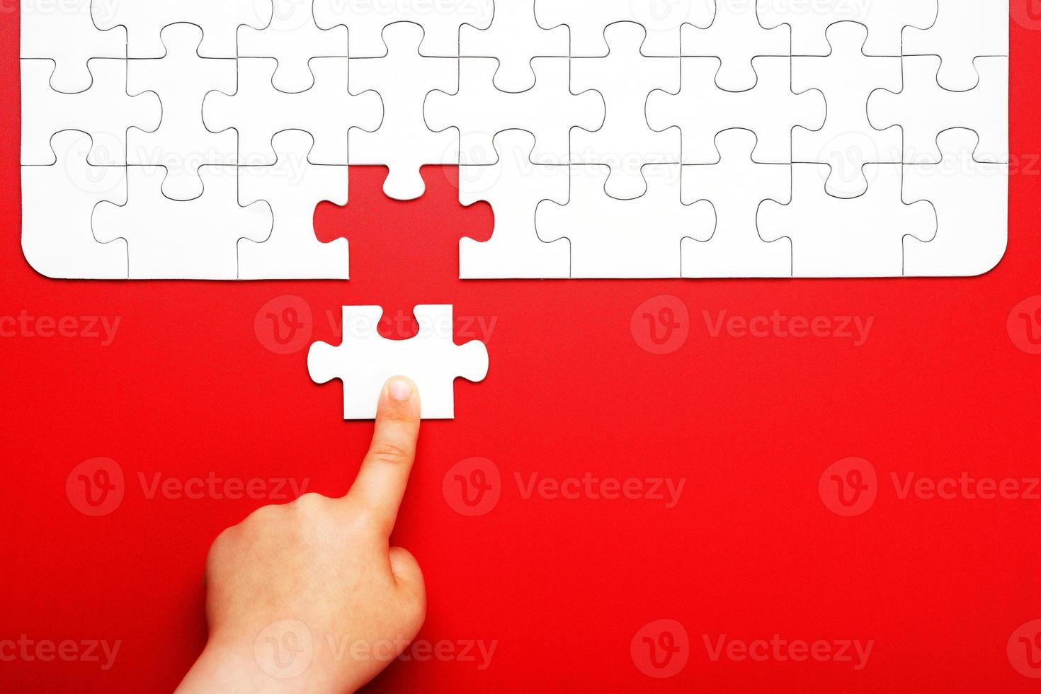 Children's hand moves a piece of white puzzle on a red background photo