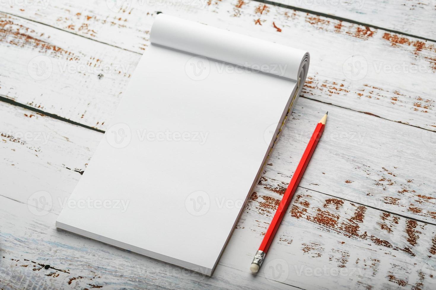 bloc de notas con un lápiz rojo sobre una mesa de madera blanca en el fondo, para educación, registro de objetivos y hechos foto