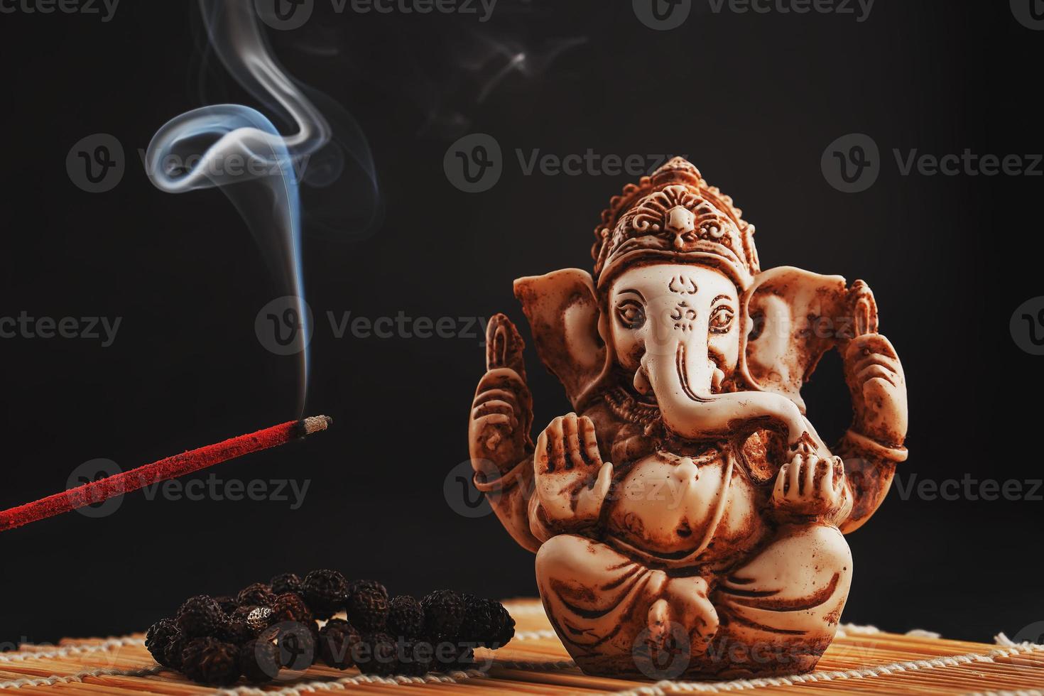 dios hindú ganesh sobre un fondo negro. estatua de rudraksha y rosario sobre una mesa de madera con un palo de incienso rojo y humo de incienso foto