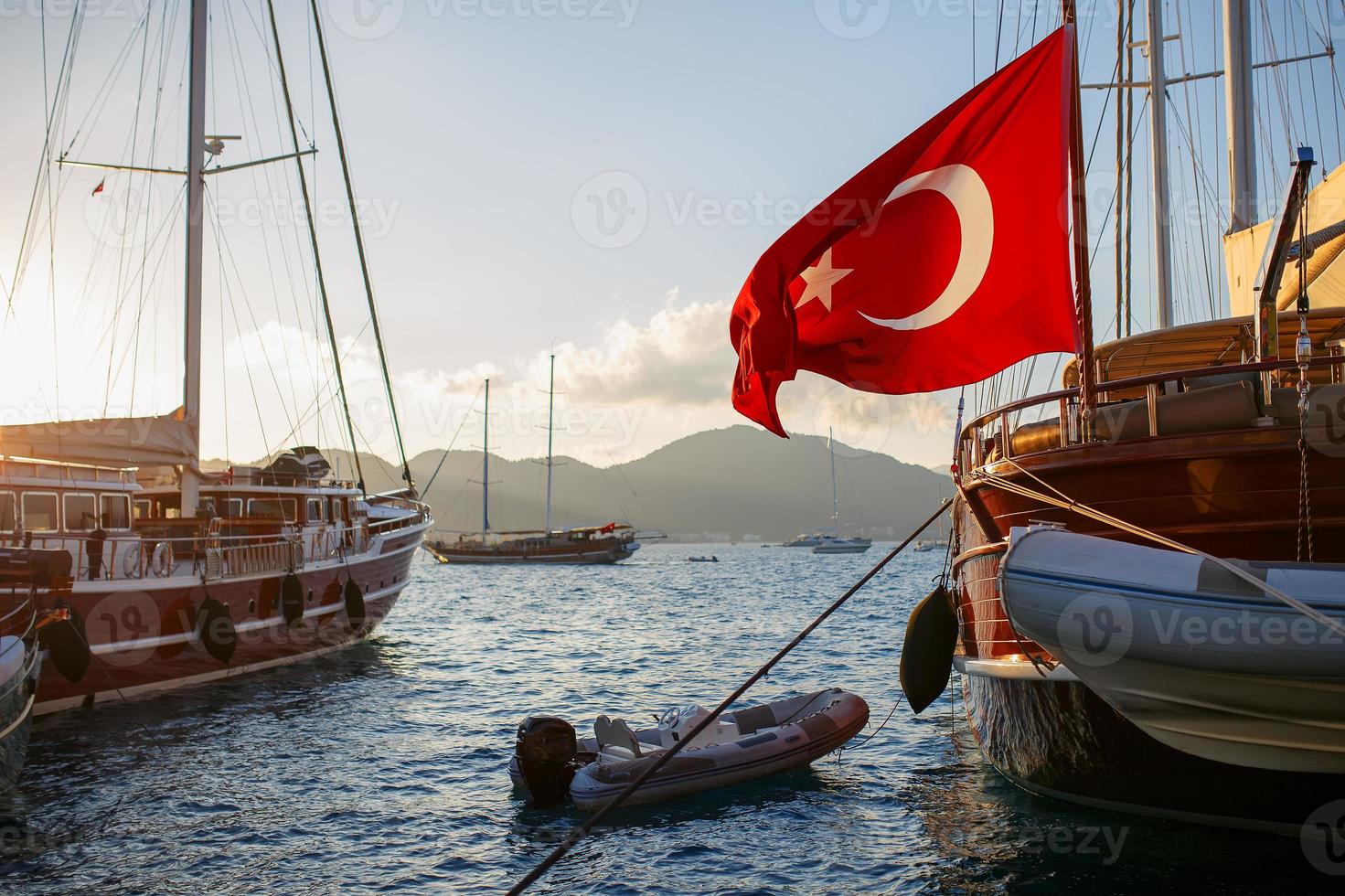 hermoso yate de madera con la gran bandera de Turquía en el muelle, con el telón de fondo de un hermoso cielo de puesta de sol con rayos de sol foto
