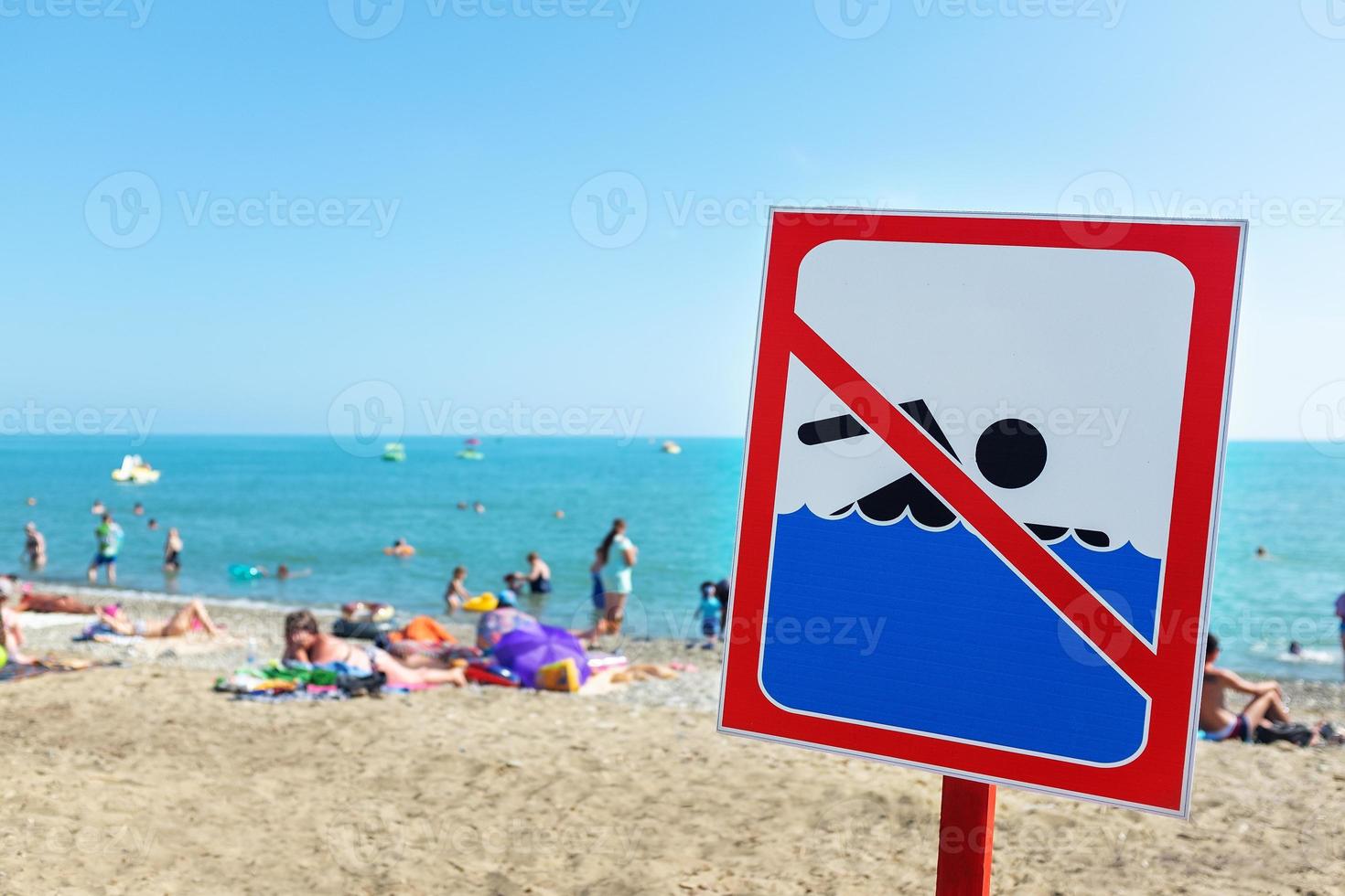 una señal en la playa no está permitida para nadar, la gente se baña y descansa en el mar a pesar de la señal y la prohibición. foto