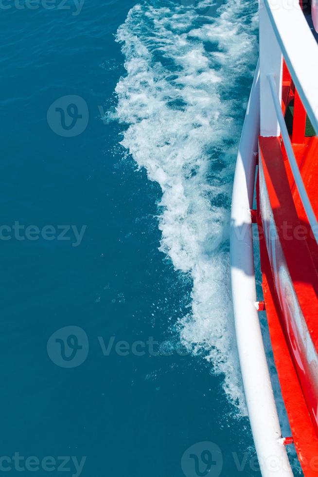 The red side of the cruise ship cuts through the blue sea surface, leaving the waves photo