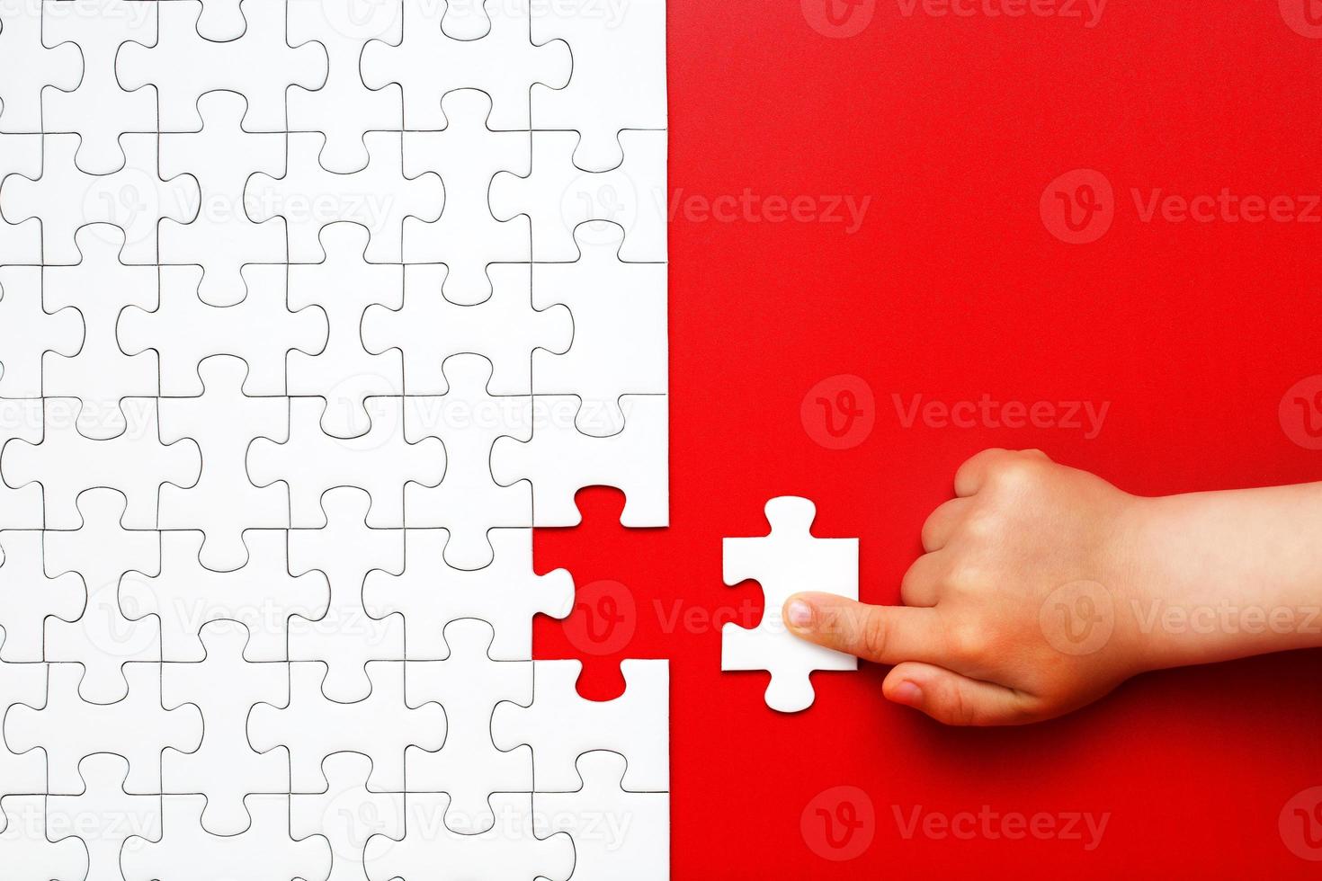 Children's hand moves a piece of white puzzle on a red background photo