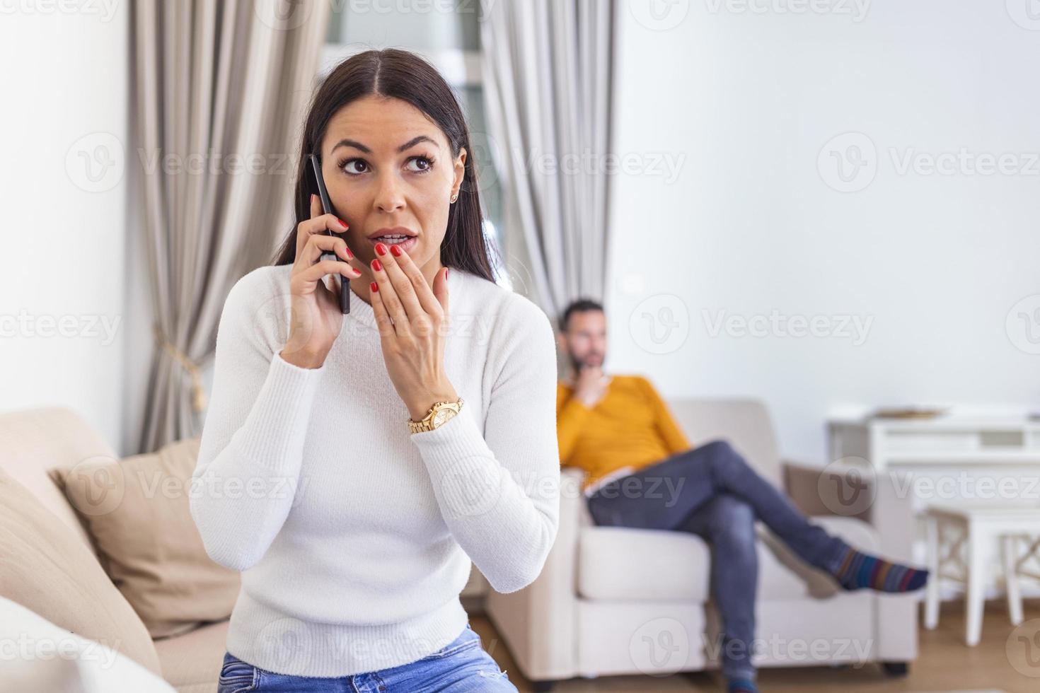 Woman turned her back to man, talking on phone with her lover, boyfriend sitting in the back watching tv. Cheating and infidelity concept photo