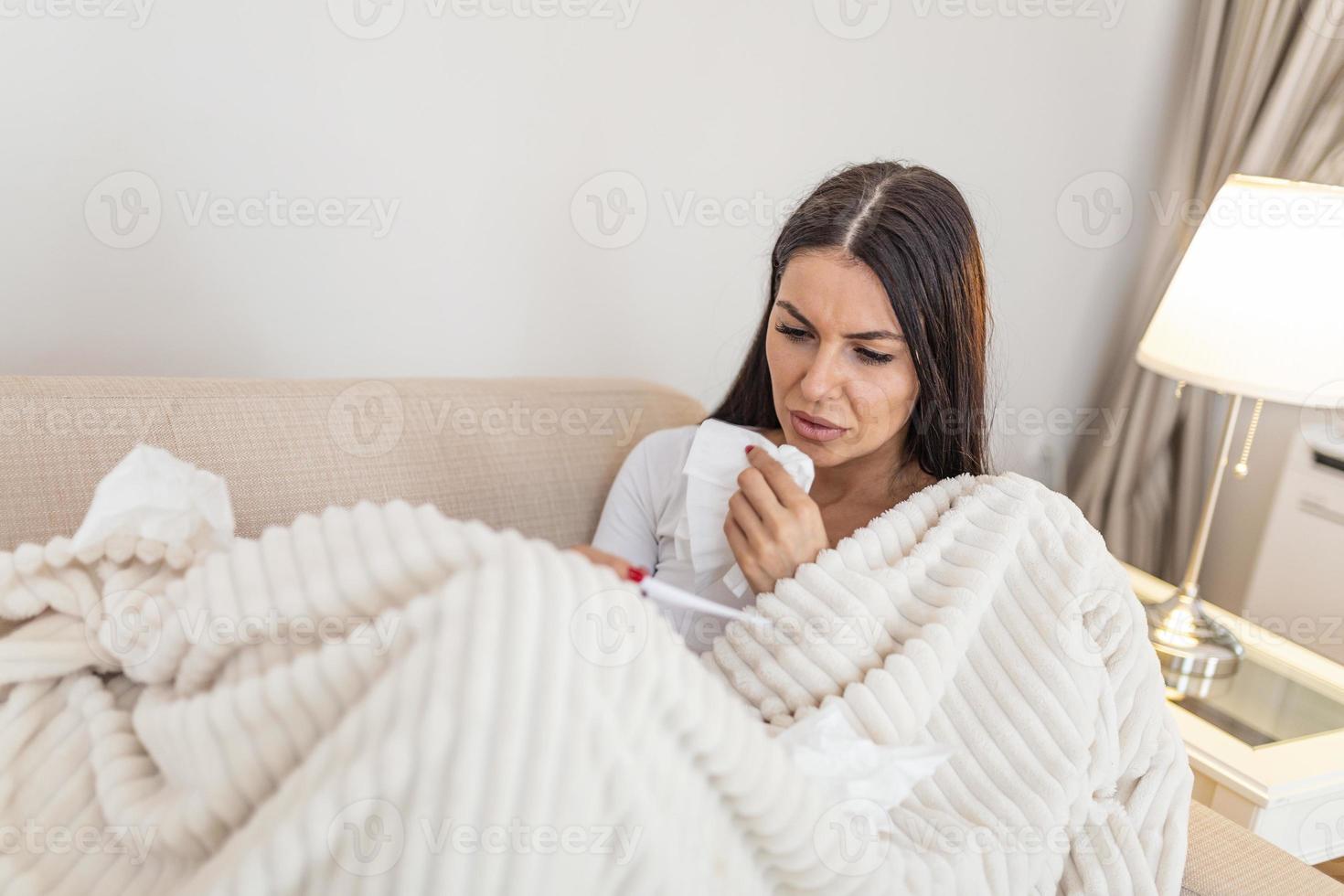 Sickness, seasonal virus problem concept. Woman being sick having flu lying on sofa looking at temperature on thermometer. Sick woman lying in bed with high fever. Corona Virus photo