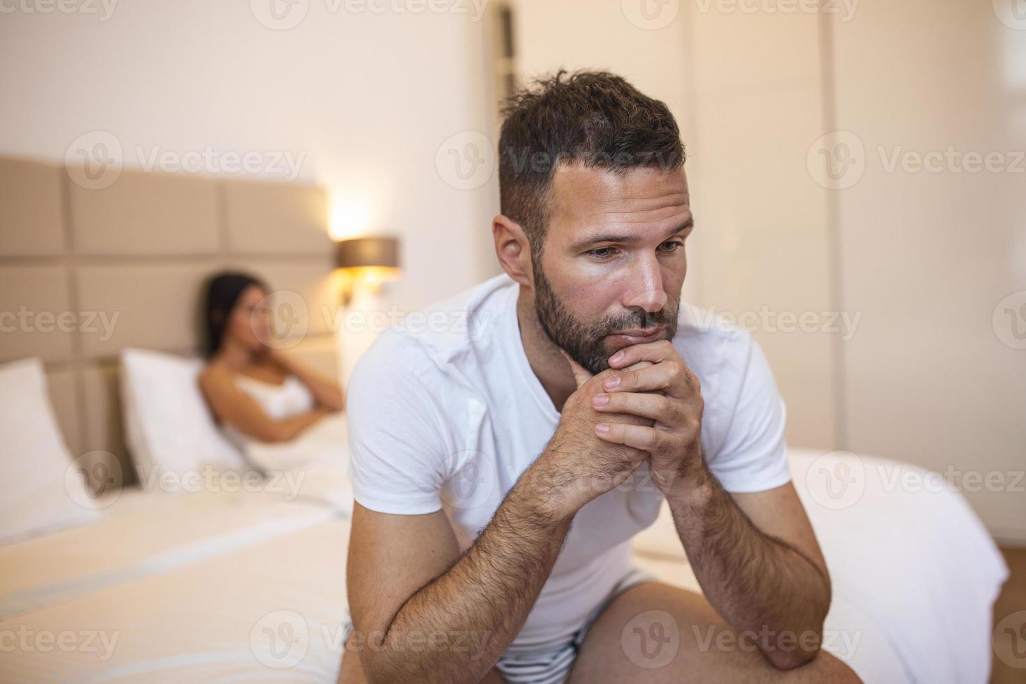 Beautiful girl and a frustrated man sitting in bed and not looking at each other. Upset couple ignoring each other. Worried man in tension at bed. Young couple angry with each other after a fight. photo