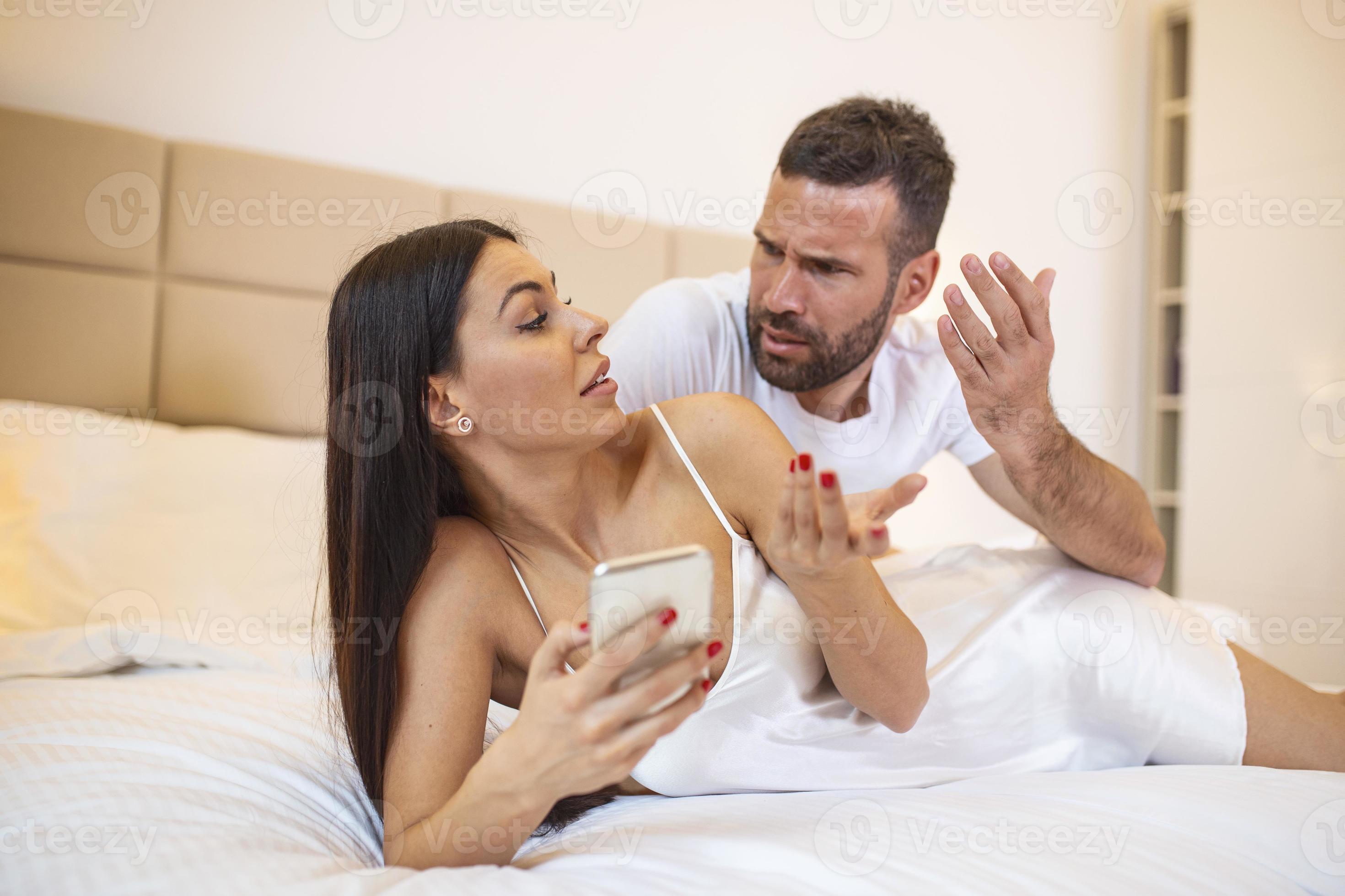 Photo of young couple in bed, woman use smartphone try explain envy angry husband she dont have another man point hand screen feel confused