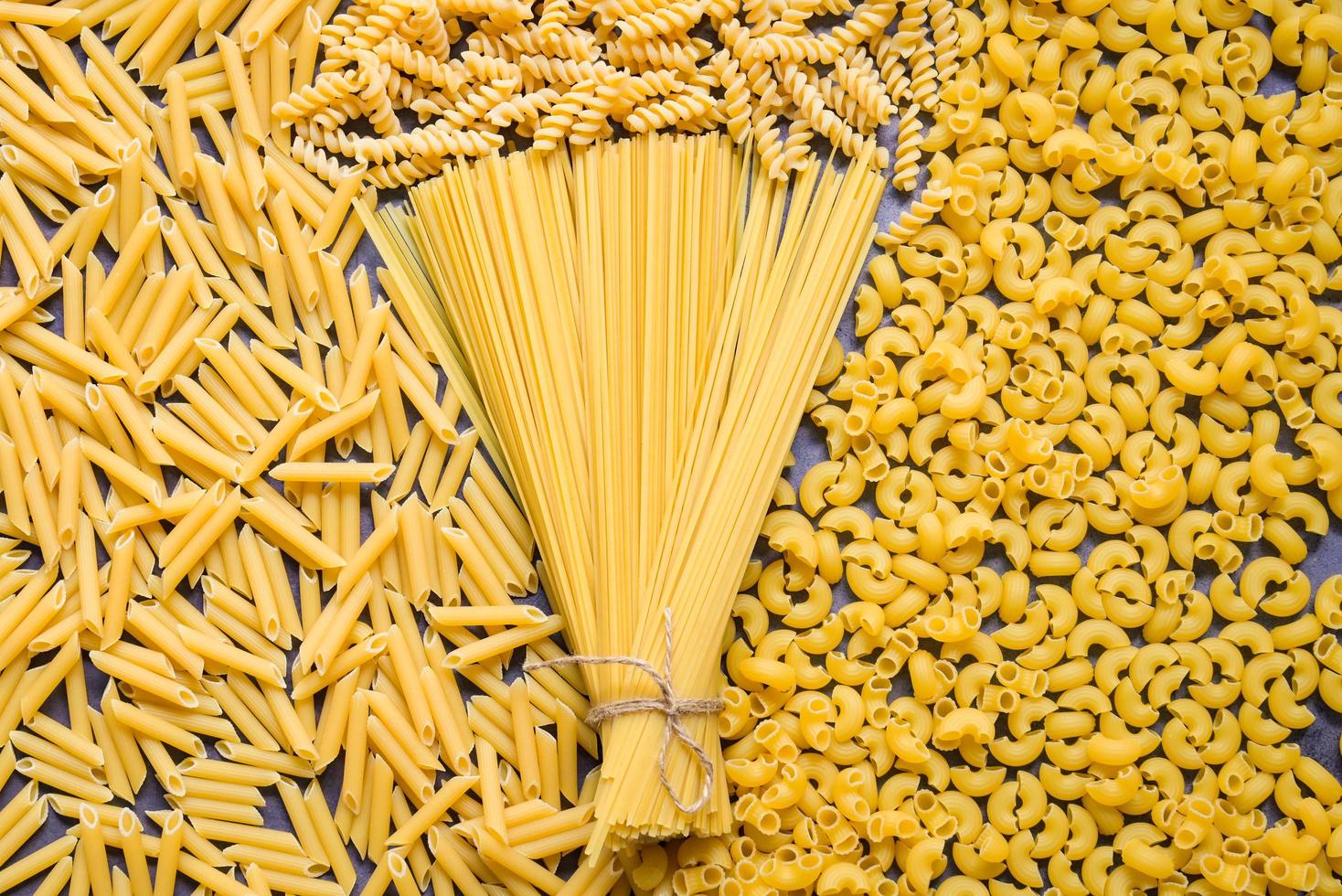 Raw pasta various kinds of uncooked pasta macaroni spaghetti and noodles on background - top view, Italian food culinary concept, Collection of different raw pasta on cooking table for cooking food photo