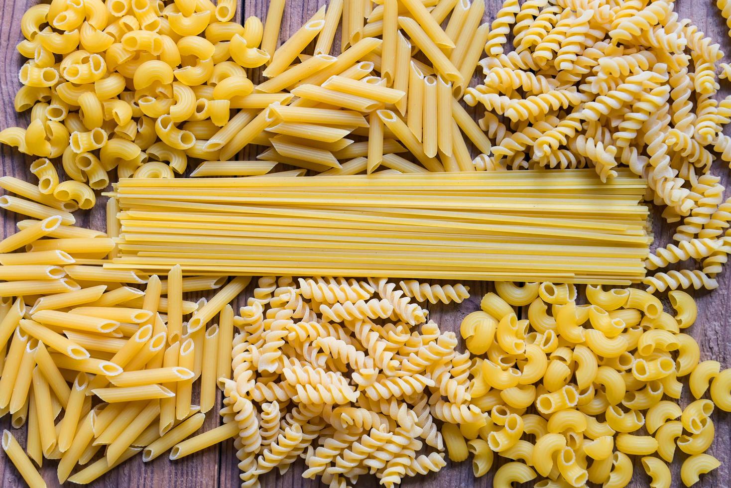Raw pasta various kinds of uncooked pasta macaroni spaghetti and noodles on wooden - top view, Italian food culinary concept, Collection of different raw pasta on cooking table for cooking food photo
