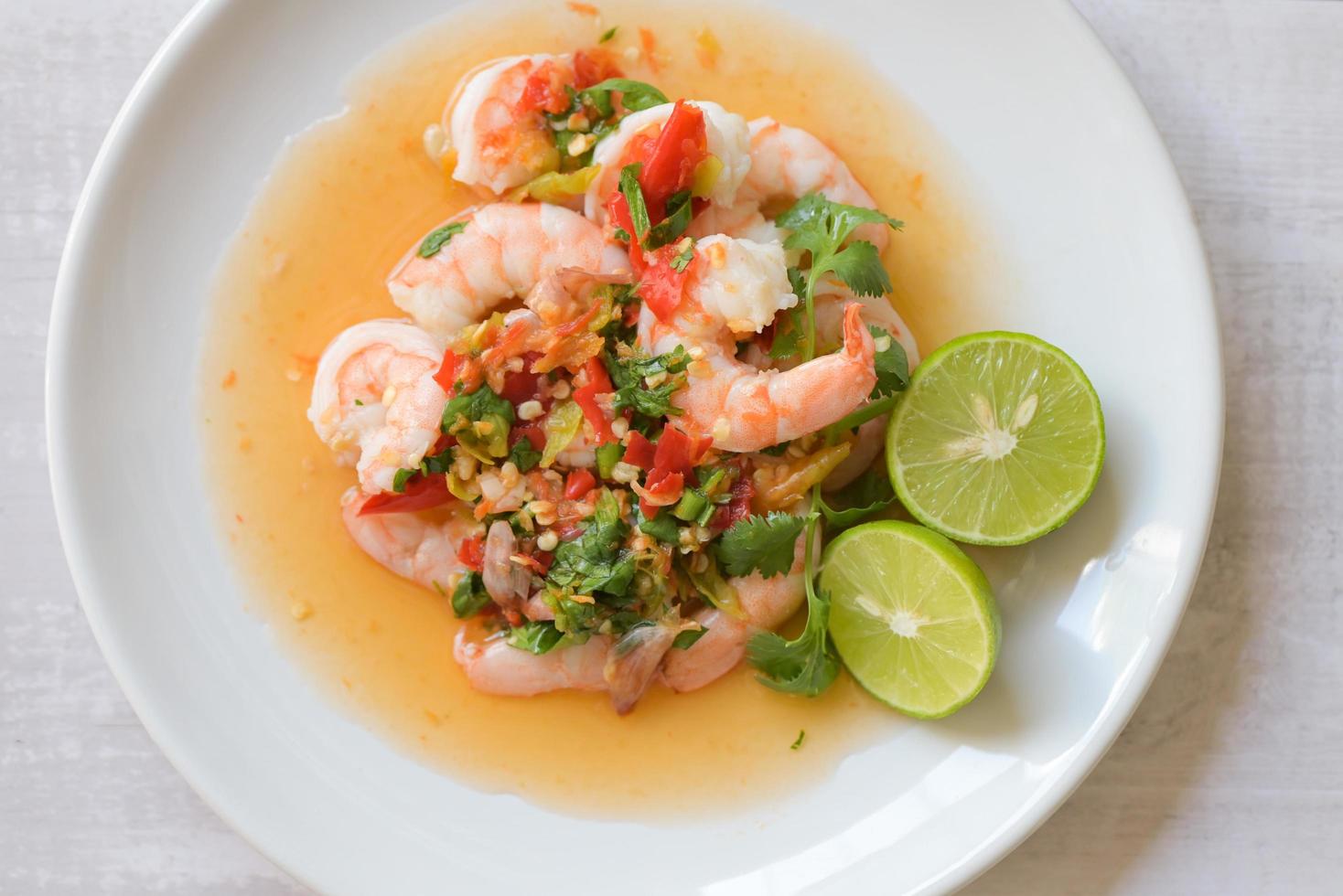 Fresh shrimp on white plate and fresh vegetables, cooked shrimps prawns and seafood spicy chili sauce coriander, cooking shrimp salad lemon lime - top view photo