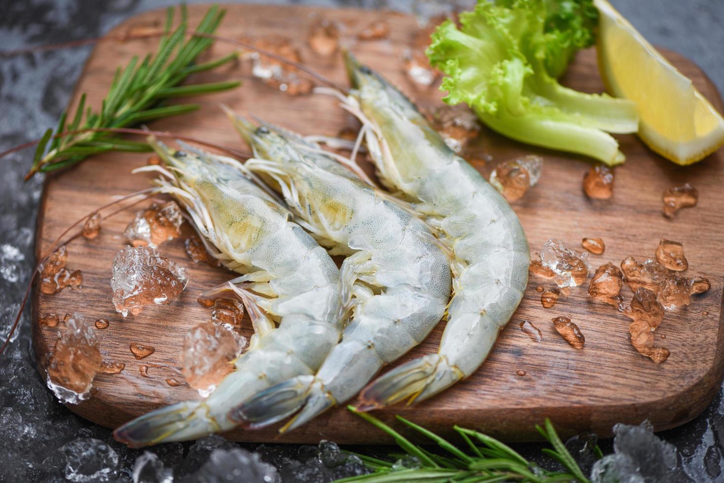 Raw shrimps prawns on ice frozen at the seafood restaurant - fresh shrimp on wooden cutting board with rosemary ingredients herb and spices for cooking seafood photo