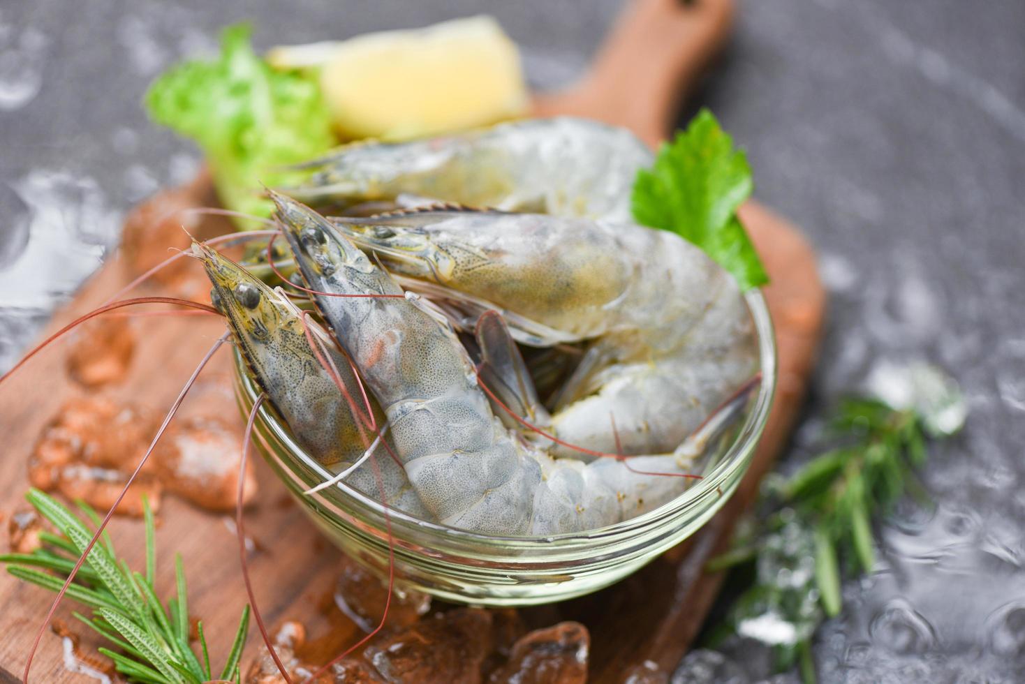 gambas gambas crudas sobre hielo congeladas en el restaurante de mariscos - gambas frescas en un tazón y tabla de cortar de madera con ingredientes de romero, hierbas y especias para cocinar mariscos foto