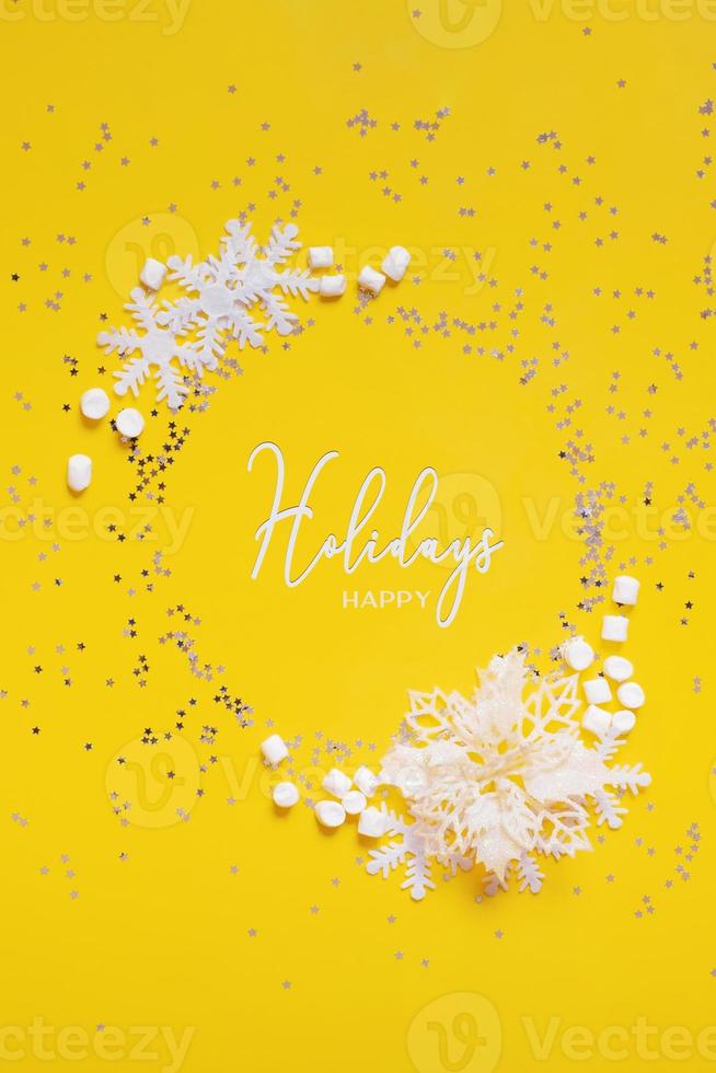 Happy Holidays text in frame made from snowflakes, marsh mellow and puansettia on yellow background. Vertical forma photo