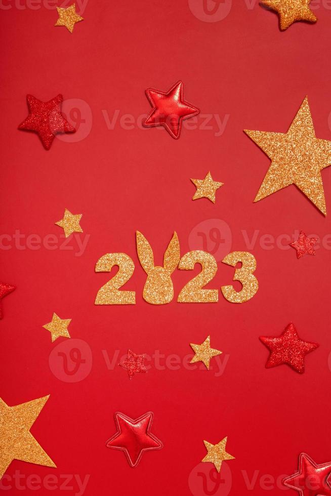 2023 new year flat lay creative concept. Numbers 2023 with rabbit ears, red and gold stars, top view on red background photo