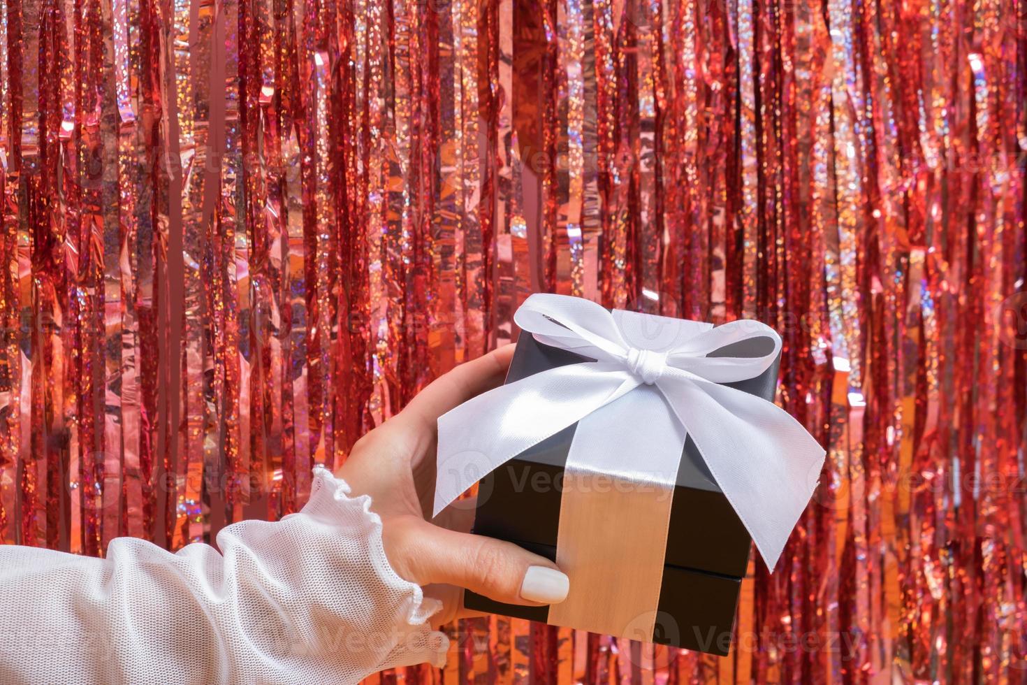 feliz navidad y feliz año nuevo concepto con mano femenina con caja de regalo en el fondo de la fiesta foto