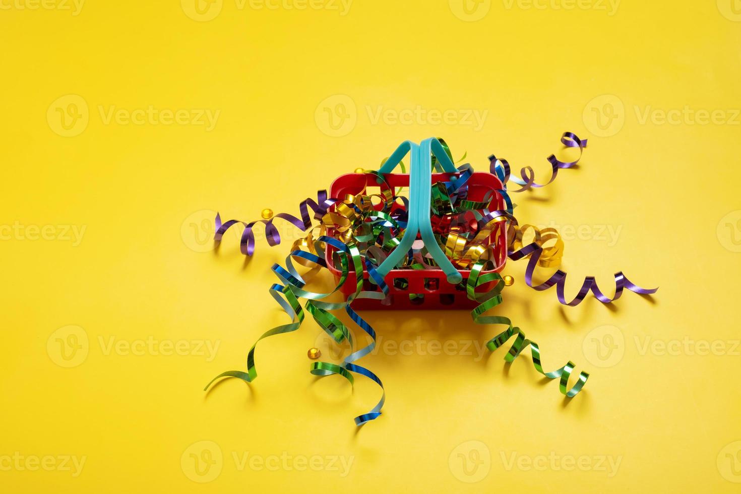 Doll's shopping basket with festive colorful tinsel on yellow background photo