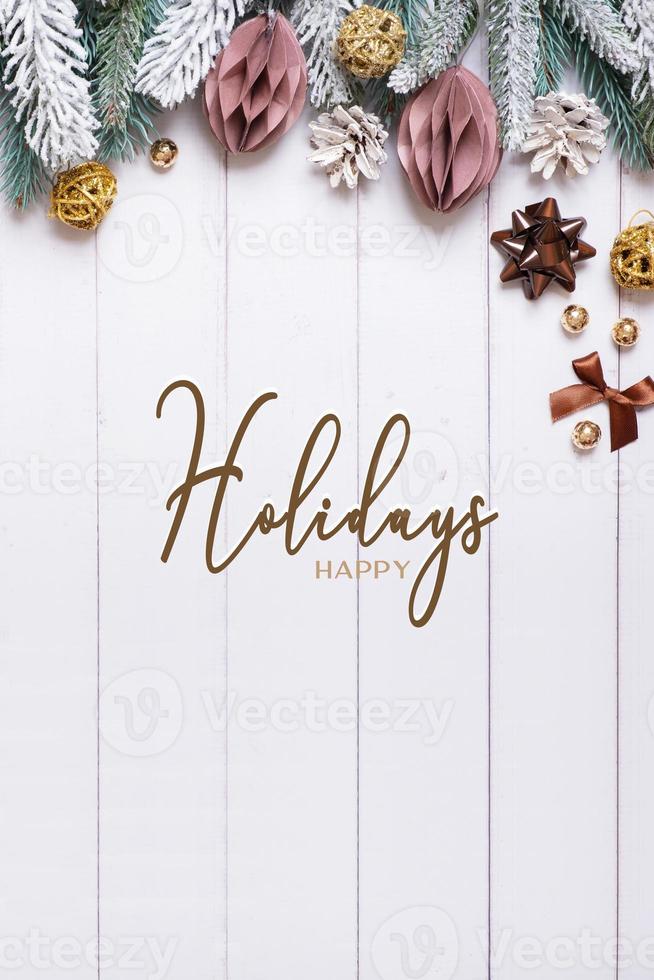 Happy holidays text on vertical wooden background with flat lay snow pine trees, paper Christmas balls photo