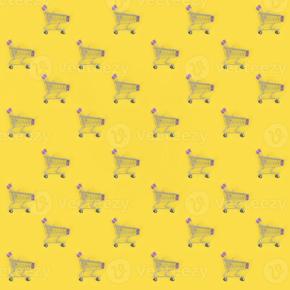 Shopping addiction, shopping lover or shopaholic concept. Many small empty shopping carts perform a pattern on a pastel colored paper background. Flat lay composition, top view photo