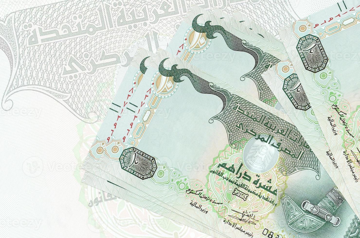 10 UAE dirhams bills lies in stack on background of big semi-transparent banknote. Abstract presentation of national currency photo