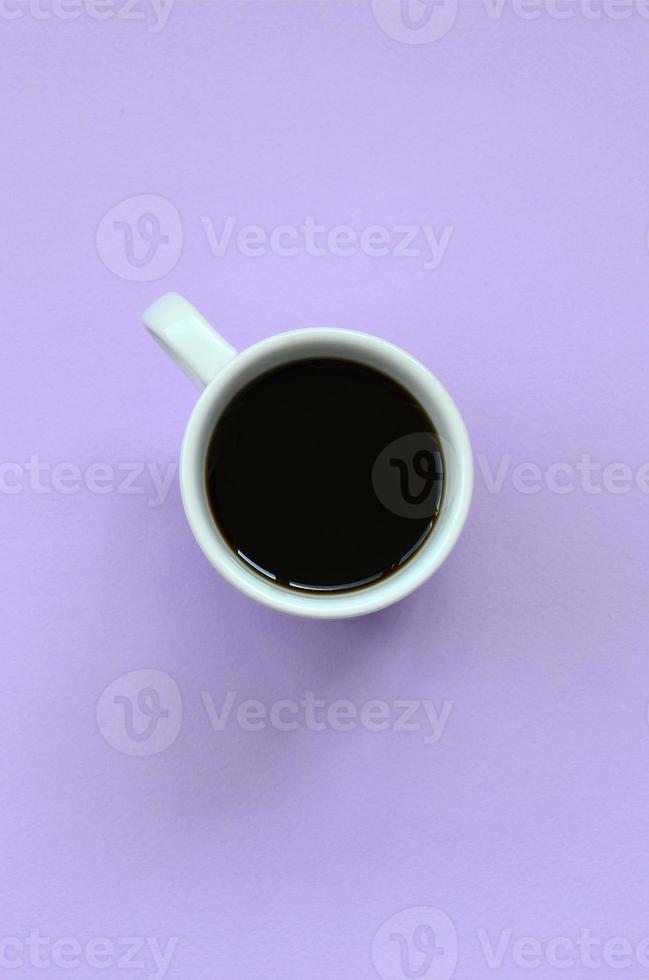 pequeña taza de café blanca sobre fondo de textura de papel de color violeta pastel de moda en concepto mínimo foto