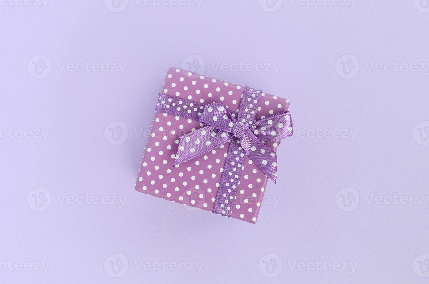 Small purple gift box with ribbon lies on a violet background. Minimalism flat lay top view photo