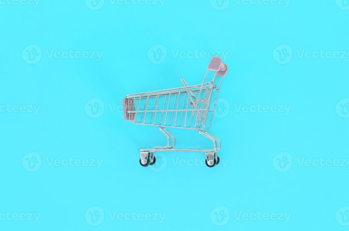 Shopping addiction, shopping lover or shopaholic concept. Small empty shopping cart lies on a pastel colored paper background. Flat lay minimal composition, top view photo