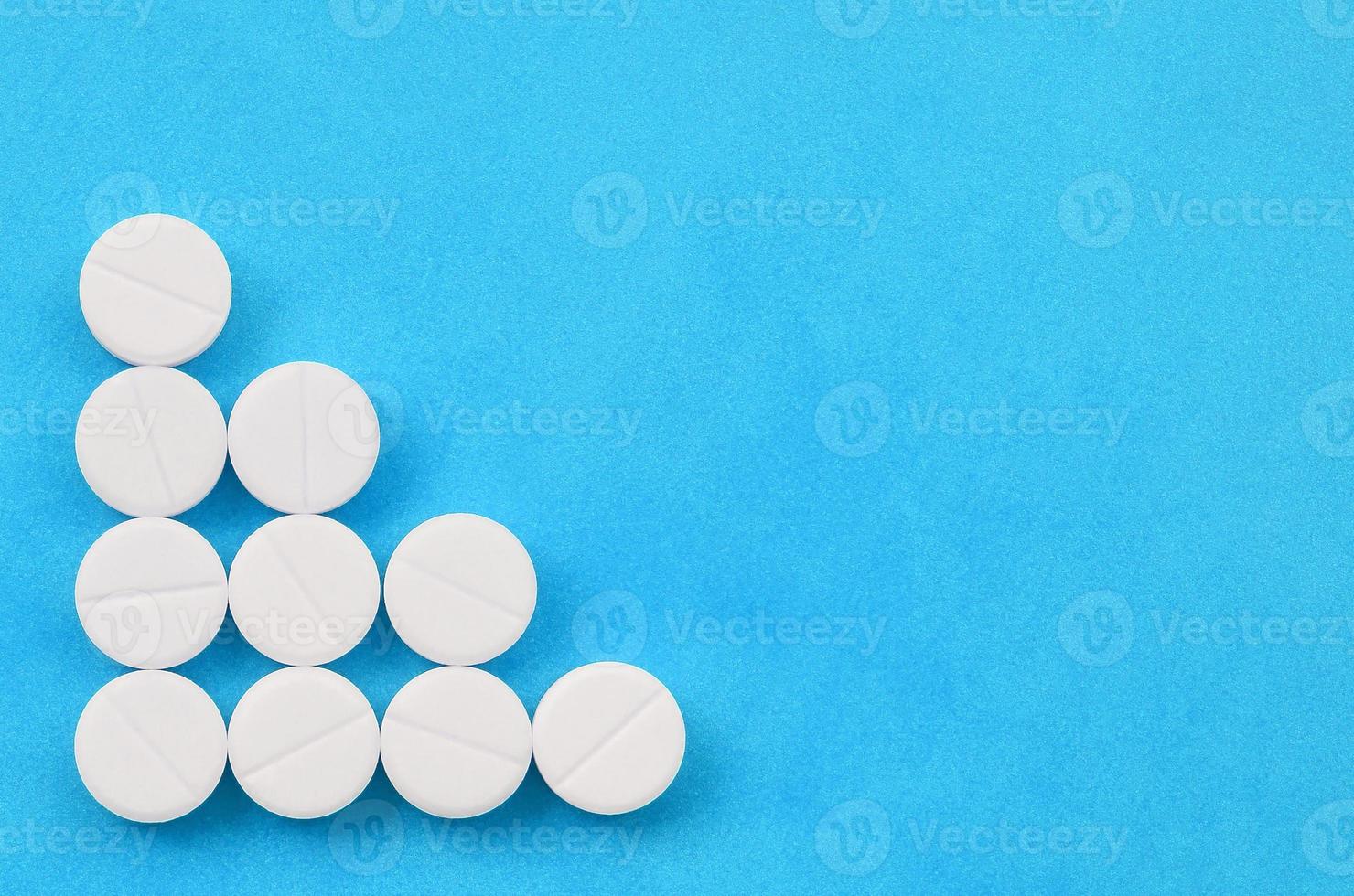 Several white tablets lie on a bright blue background in the form of a triangular arrow. Background image on medicine and pharmaceutical topics photo