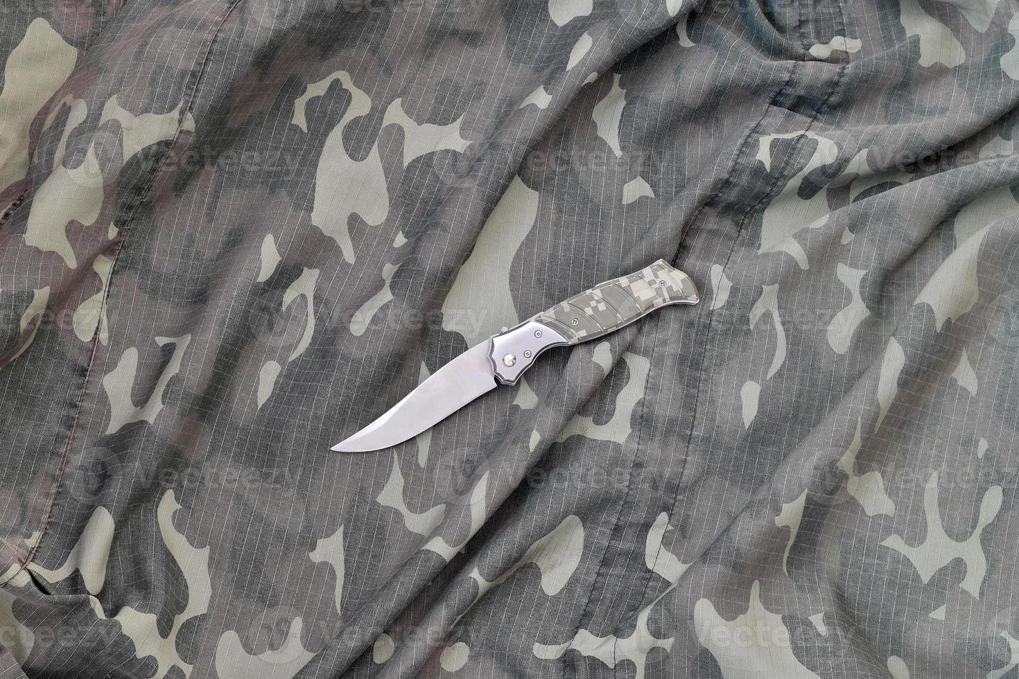 Military knife on army camouflage clothes close up. Background with copy space for military or special service design photo