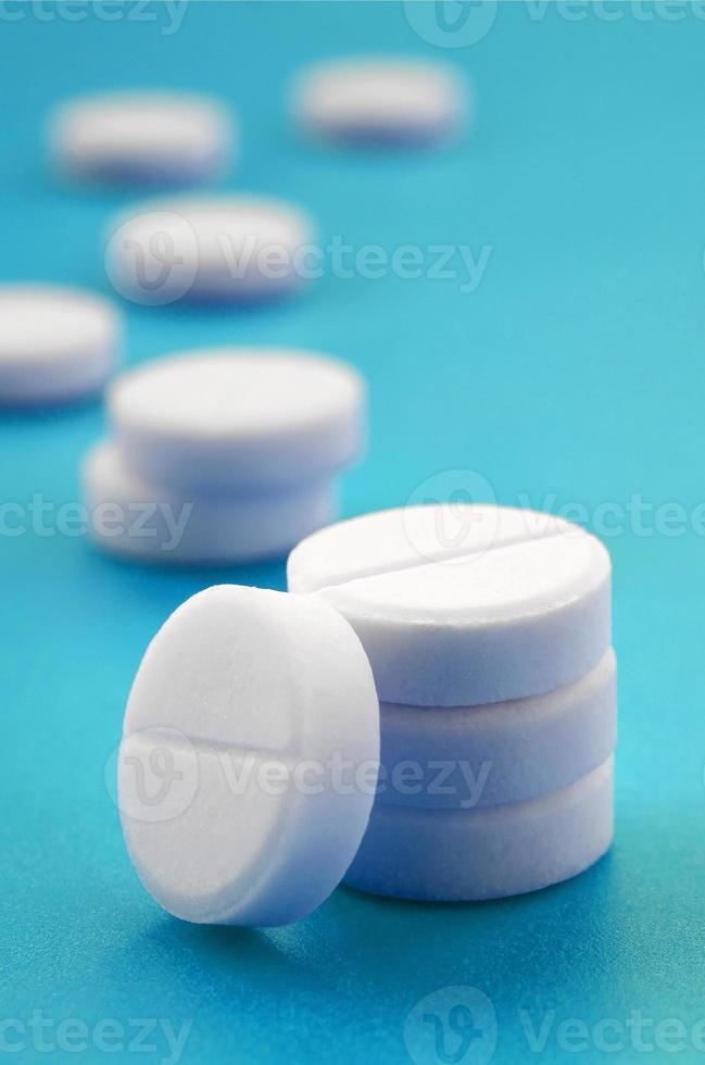 A few white tablets lie on a bright blue background surface. Background image on medical and pharmaceutical topics photo