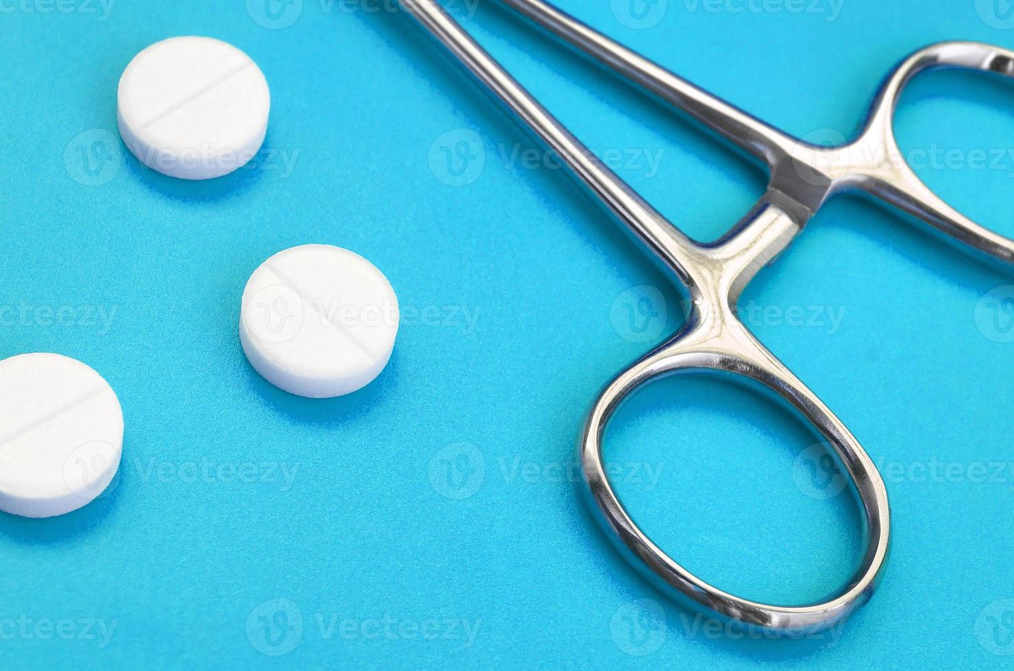 Several white tablets and a medical clamp lie on a bright blue background surface. Background image on medical and pharmaceutical topics photo