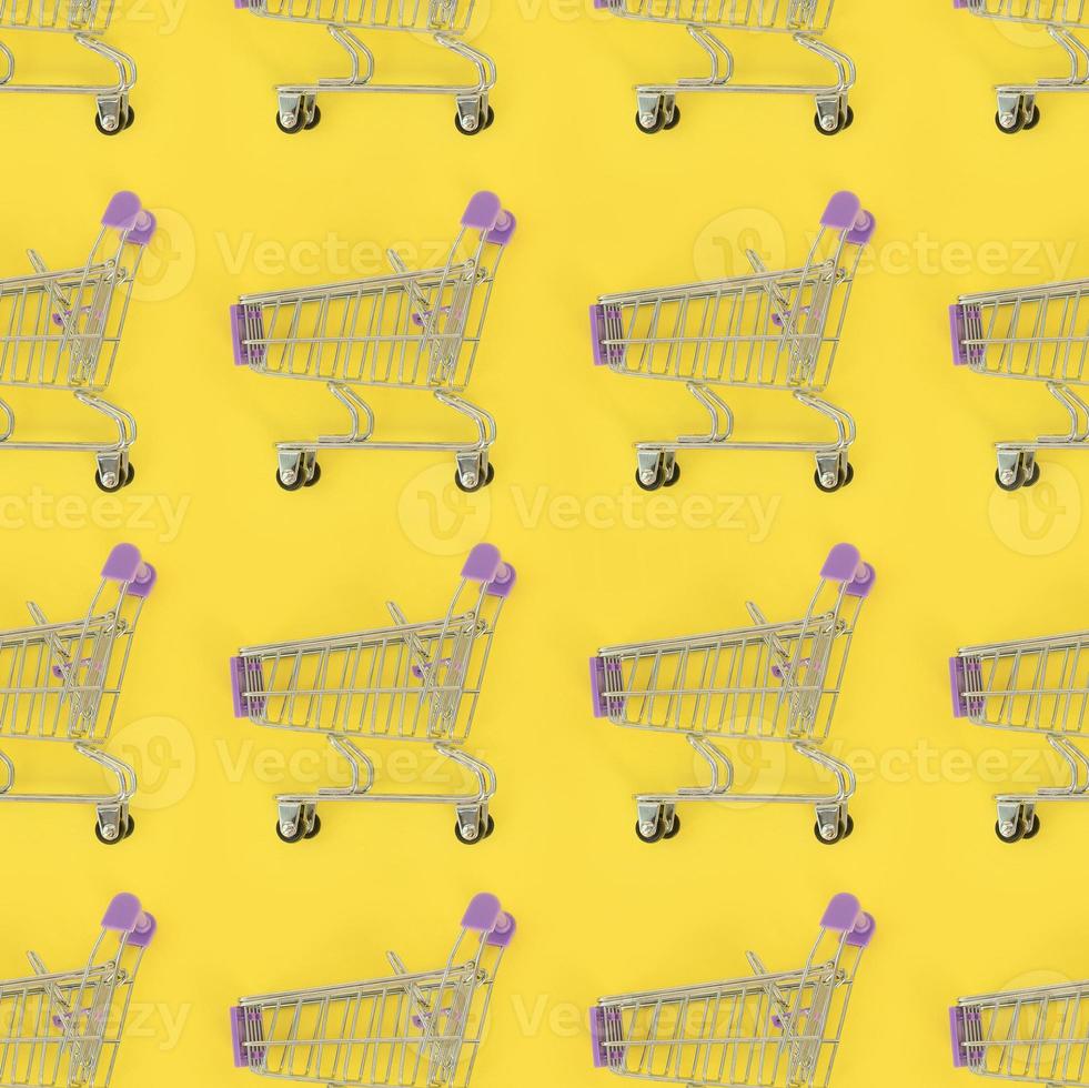 Shopping addiction, shopping lover or shopaholic concept. Many small empty shopping carts perform a pattern on a pastel colored paper background. Flat lay composition, top view photo