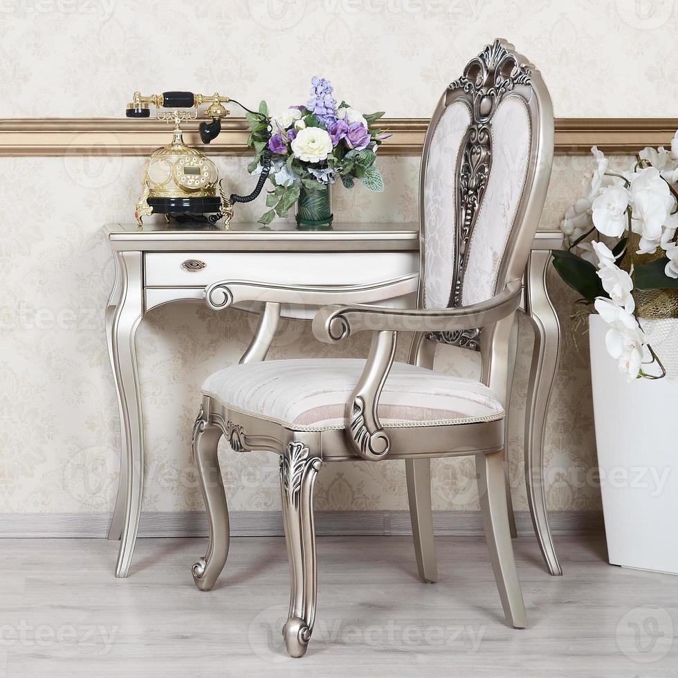 A fragment of a retro interior with a chair and a desk on which is located a telephone and a vase of flowers photo