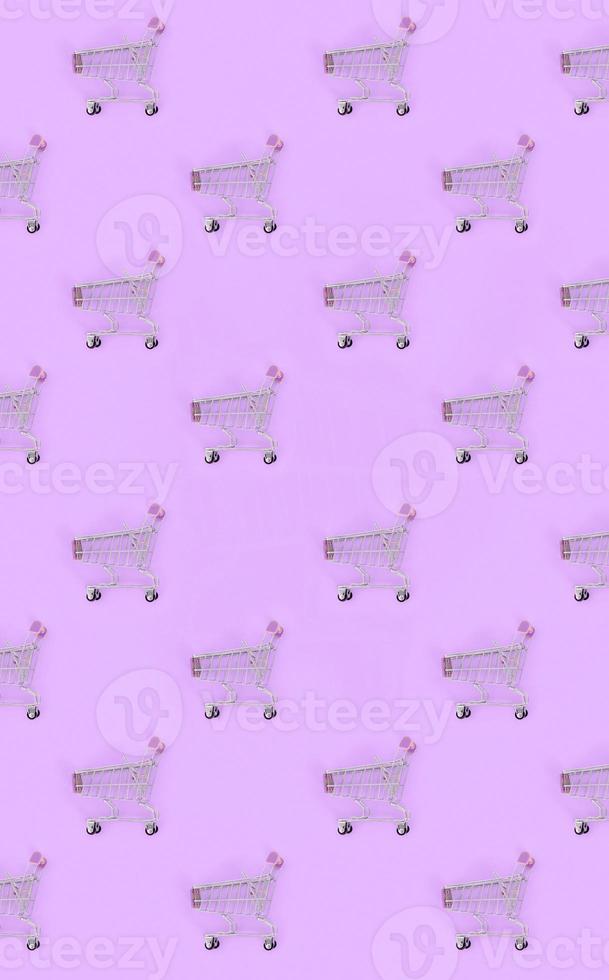 Shopping addiction, shopping lover or shopaholic concept. Many small empty shopping carts perform a pattern on a pastel colored paper background. Flat lay composition, top view photo