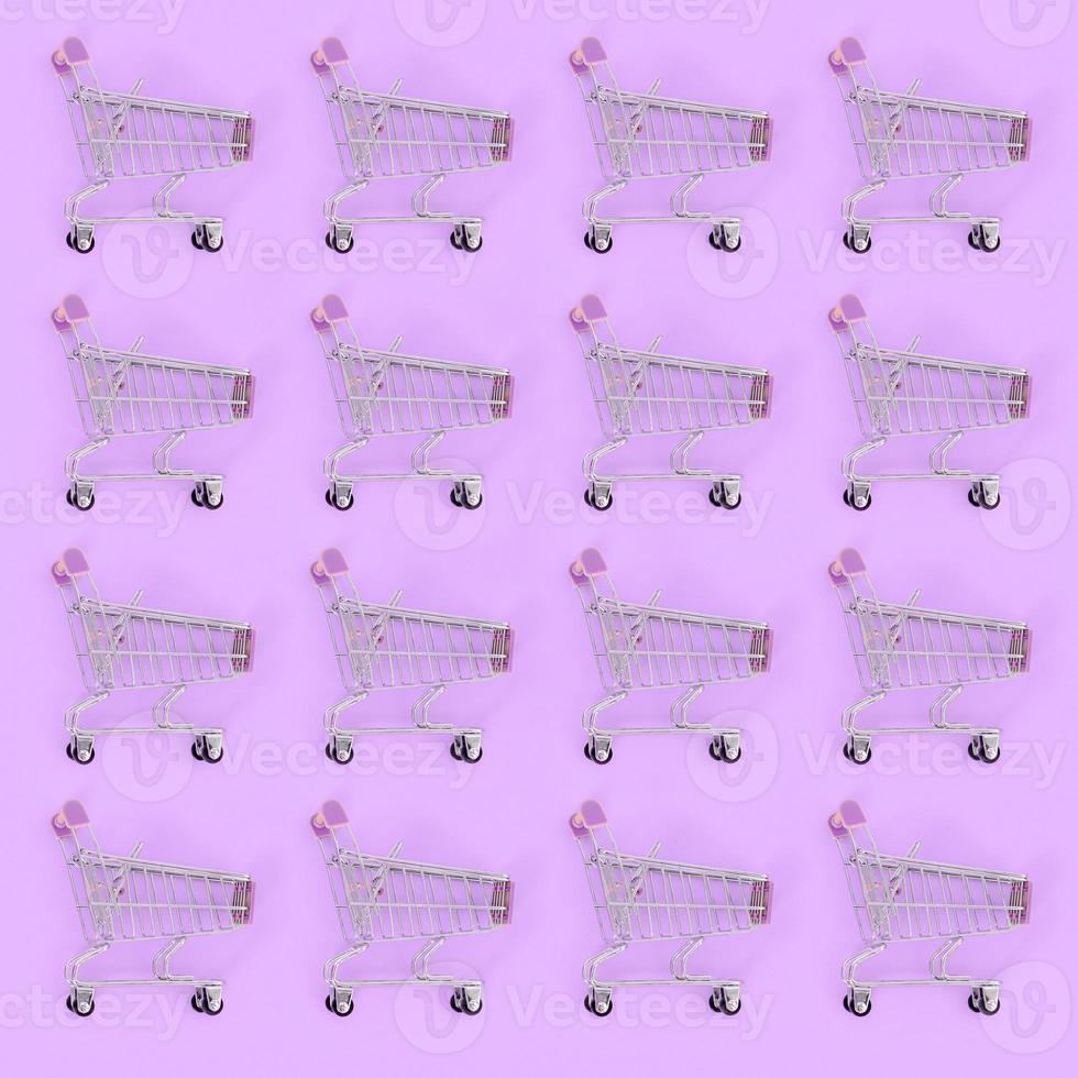 Shopping addiction, shopping lover or shopaholic concept. Many small empty shopping carts perform a pattern on a pastel colored paper background. Flat lay composition, top view photo